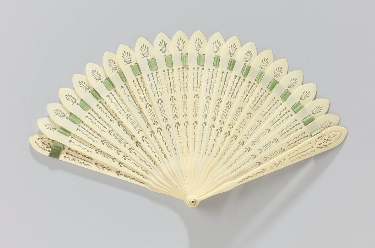 Brisé fan of openwork carved bone, held together with a green satin ribbon