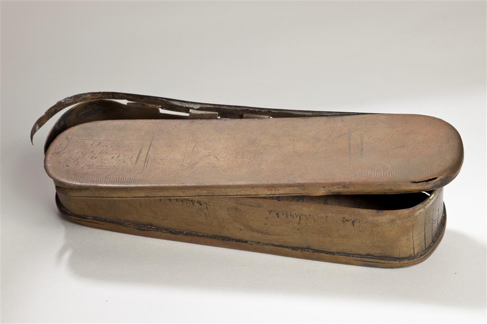 A worn copper tobacco box whose lid has come half loose. On the lid (unrecognizable) figures are depicted and to the left and right of this (illegible) text is ap