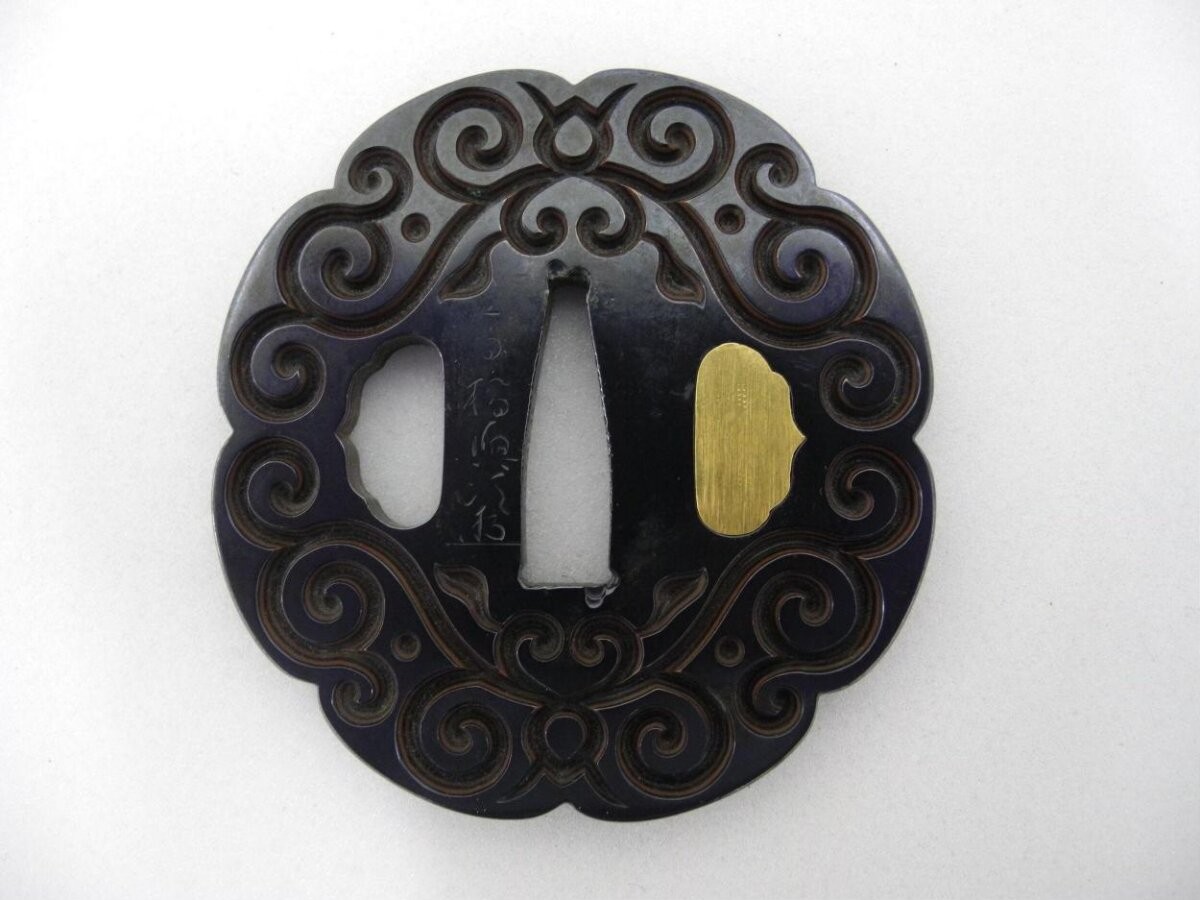 Sword guard (tsuba) with carved design of scrollwork in guribori style; signed ‘Takahashi Okitsugu’ with art signature (kakihan).