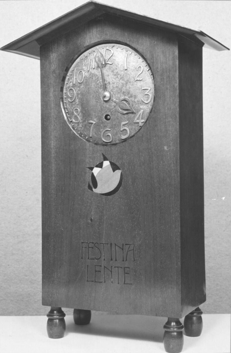 CLOCK Mahogany case inlaid with coloured woods, the inlay including the inscription 'FESTINA LENTE'. The dial of copper Designed by Mackay Hugh Baillie Scott Made by J P White, The Pyghtle Works, Bedford, about 1900