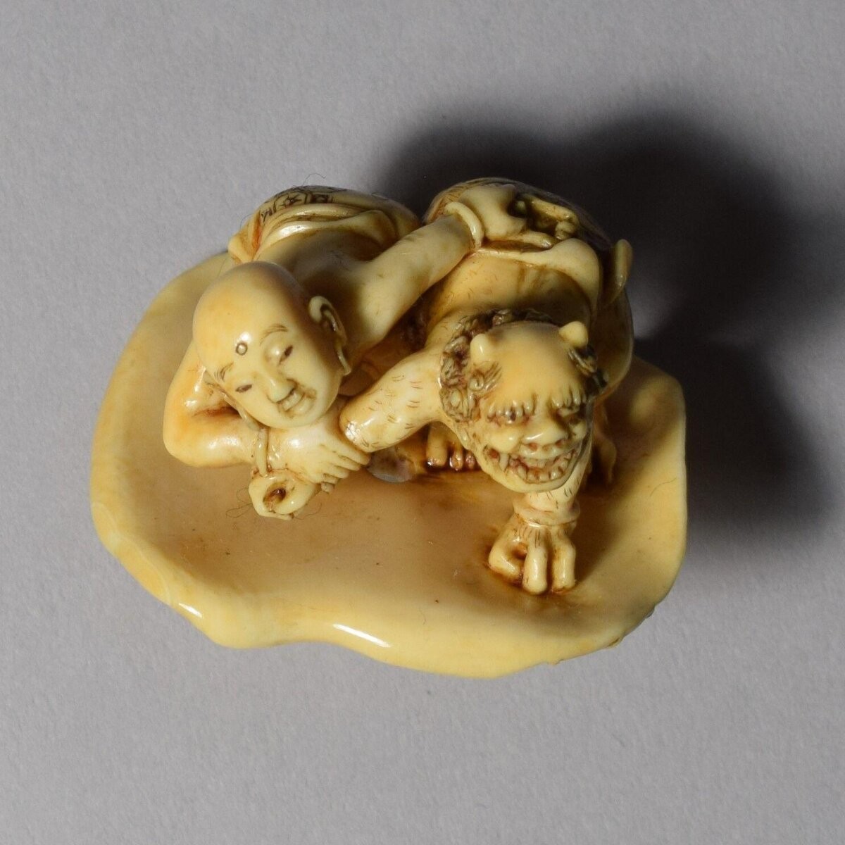 Netsuke in ivory of an oni (demon) wrestling with a Chinese child on a lotus leaf, signed Ho Kiokumin, 18th century, Japan