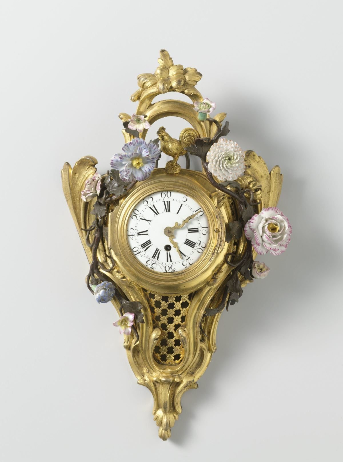 Cartel clock of gilt bronze with round dial decorated with rocailles and painted metal leafy branches with porcelain flowers.