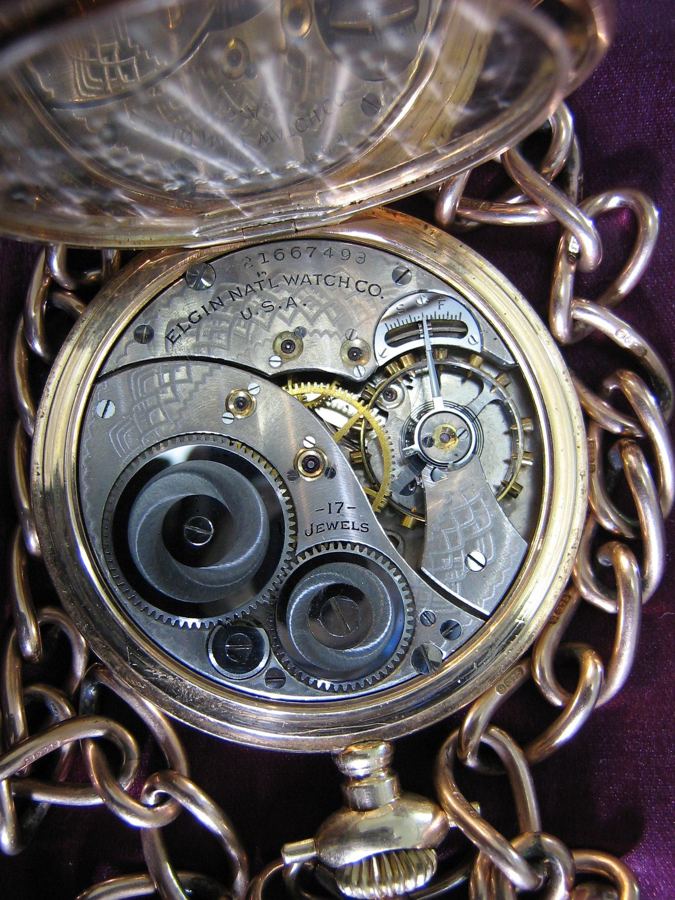 A gold pocket watch made by the Elgin National Watch Company of Elgin, Illinois, cir.1919, with the back open showing the movement of the watch. There is an inscription on the inside back cover "Presented by Esquesing Township and Citizens of Glen Williams to Private Wilson Heato